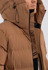 Braune Daunenjacke mit hohem Kragen, verstellbarem Kapuzenrand, schwarzem Reißverschluss und Innendetails mit Branding. Der Oberstoff ist glatt und gepolstert.
