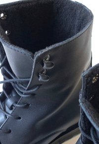 Botas de cuero negras con un alto collar de fieltro suave. Las características incluyen cordones redondos negros, dos ojetes metálicos y un acabado suave.