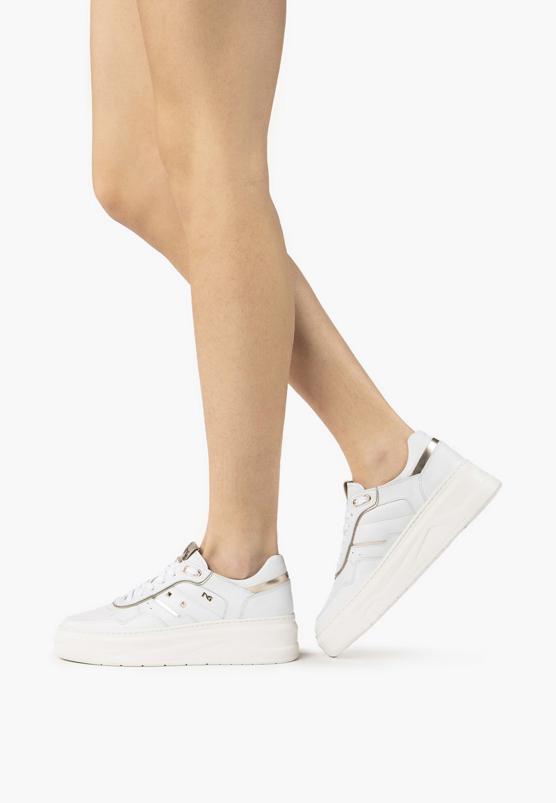 White sneakers with a textured leather upper, gold accents, and a thick white sole. Lace-up design with padded collar and side detailing.