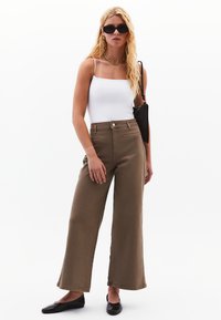 Pantaloni larghi marroni con vita alta, realizzati in tessuto testurizzato, abbinati a un top aderente bianco e accessori neri.