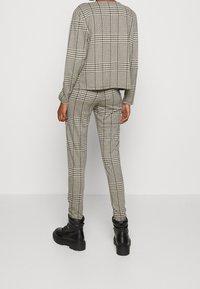Pull court à motifs à carreaux et pantalon ajusté en noir et blanc. Stylé avec des bottes noires épaisses. Mise en valeur des formes géométriques et des textures.