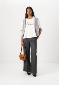 White graphic t-shirt with "COWGIRLS" text, gray vest, gray striped trousers, and a brown crossbody bag. Black shoes complete the look.