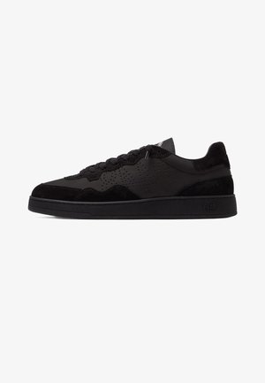 Low-top black sneaker with suede and perforated leather panels, black laces, and a thick black sole with subtle branding on the heel.