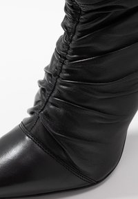 Schwarze Leder-Stiefelette mit spitzer Zehe und gerafftem Design. Sie verfügt über eine glatte Textur mit einer schlanken, modernen Silhouette und minimalen Nähte.