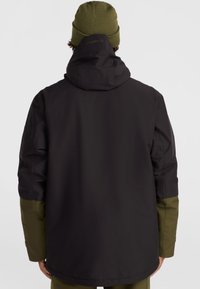 Veste imperméable noire avec des manches vert olive, dotée d'une capuche et d'un logo sur le col. Texture lisse et coupe ajustée.