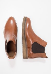 Brown leather ankle boots with elastic side panels, rounded toe, and textured rubber sole. Features stitching along the edge.