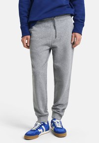 Grå bomulds joggingbukser med elastisk talje og snøre, der har sidelommer og en afslappet pasform. Stylet med blå og hvide sneakers.