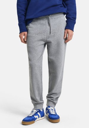 Šedé bavlněné tepláky s elastickým pasem a šňůrkou, s bočními kapsami a volným střihem. V kombinaci s modro-bílými teniskami.