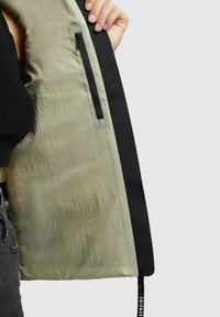 Green and black jacket interior, featuring a textured, light green fabric with a zipper pocket and a black trim along the edge.