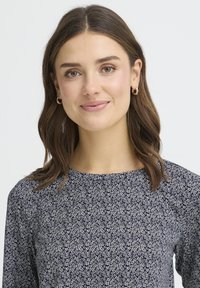 Marineblå blomstret top med rund halsudskæring, med små hvide blomster, lange ærmer og blødt, tekstureret stof.