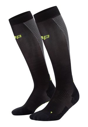 Calze a compressione con design in rete nera, caratterizzate da una texture rigata e accenti riflettenti grigi. Logo giallo brillante sulla parte superiore.