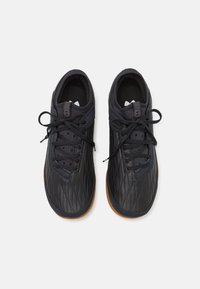 Scarpe sportive nere con una texture trapuntata, punta tonda, suola in gomma e lacci piatti con un pannello scuro a contrasto sul colletto.