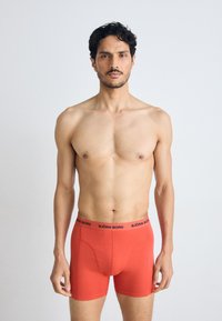 Rote Boxer Shorts mit einem schwarzen Bund, der das Logo "BJÖRN BORG" trägt. Der Stoff ist glatt, enganliegend und dehnbar.