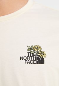 Kremfarget bomull T-skjorte med svart brodert logo og gule blomstdetaljer. Har en klassisk rund halsdesign.
