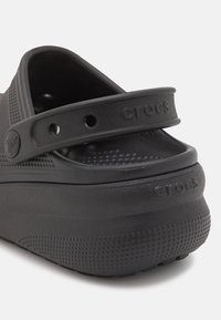 Schwarze Crocs mit robustem Design, ausgestattet mit einem perforierten Oberteil, verstellbarem Riemen, strukturiertem Oberflächen und Logo-Detail an der Ferse.