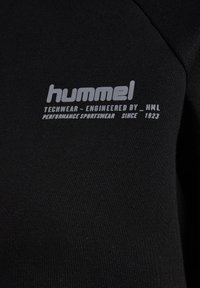 Zwarte stof met grijze tekst met de tekst "hummel TECHWEAR - ENGINEERED BY _ HML PERFORMANCE SPORTSWEAR SINCE 1923" erop gedrukt.