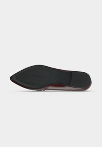Semelle d'une chaussure de ville à bout pointu en caoutchouc noir avec une adhérence texturée et un bord supérieur bordeaux lisse sur fond blanc.