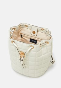 Sac seau blanc matelassé avec quincaillerie dorée, fermeture à cordon et intérieur beige clair. Comprend une poche zippée intérieure et une étiquette de logo.