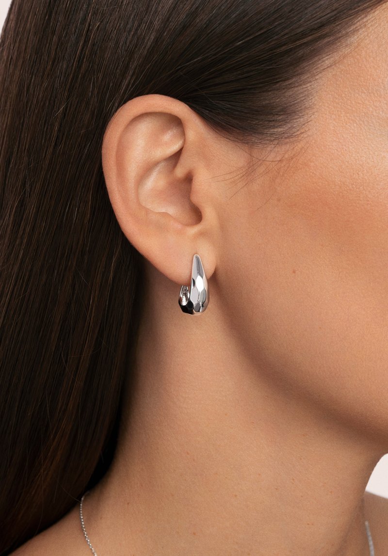 Pendientes de plata con forma de lágrima, con una superficie pulida y facetada, que refleja la luz con texturas suaves.