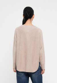 Light beige knit sweater with a round neckline, long sleeves, and a curved hem. Textured fabric shown from the back, paired with blue jeans.