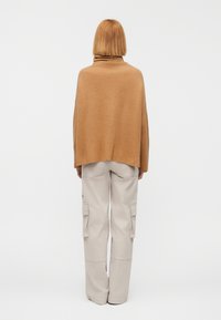 Μπρονζέ πουλόβερ με ριμπ ζιβάγκο και χαλαρή εφαρμογή, συνδυασμένο με μπεζ παντελόνι καμπαρντίνα με πλαϊνές τσέπες και άνετη σιλουέτα.
