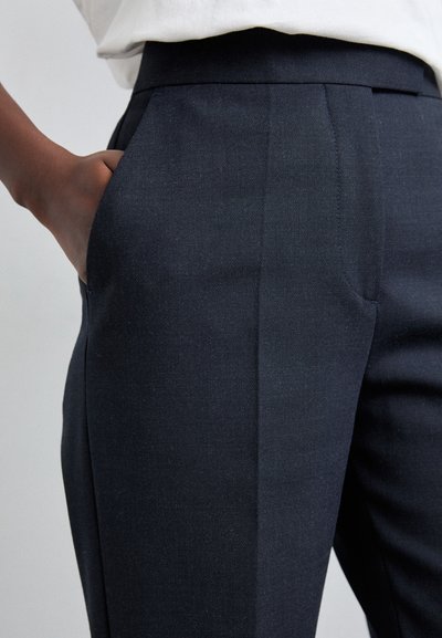 Pantaloni tailored de culoare albastru marin, cu o textură netedă, având buzunare frontale și un design cu fața plată. Betel cu o structură bine definită și ajustată.