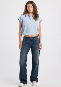 Lyhythihainen, sinivalkoraidallinen paita, jossa on leikattu helma, yhdistettynä rentoihin tummansinisiin farkkuihin. Asun viimeistelevät valkoiset lenkkarit.