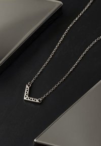 Srebrny naszyjnik z metalowym geometrycznym trójkątnym wisiorkiem z wyciętymi akcentami, zawieszony na delikatnym łańcuszku.