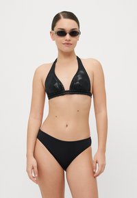 Crni bikini set s gornjim dijelom na halter koji ima sjajnu teksturu i nabran detalj, uparen s klasičnim crnim donjim dijelom gaćica.