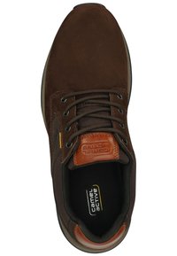 Bruine suede sneaker met donkere veters, een leren accent op de hiel en een gevoerde zwarte binnenkant. Beschikt over een ronde neus en een getextureerde zool.