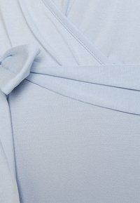 Top azul claro envolvente com textura canelada, apresentando um detalhe atado e pregas diagonais, feito de um tecido macio e elástico.