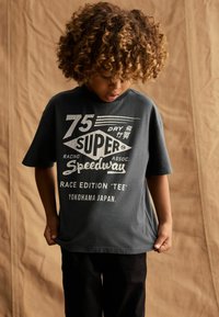 Mørkegrå bomulds t-shirt med korte ærmer, prydet med hvid grafisk tryk, der inkluderer "75 SUPER SPEEDWAY" og "YOKOHAMA JAPAN."