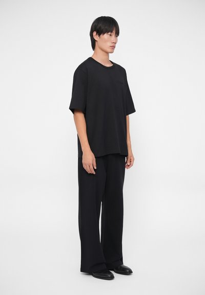 Črna kratka majica s kratkimi rokavi, izdelana iz mehkega blaga, v kombinaciji z ohlapnimi črnimi hlačami. Preprost dizajn z sproščenim silhuetom.