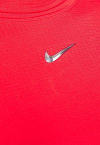 Czerwona koszulka sportowa z teksturowanej tkaniny, okrągłym dekoltem i odblaskowym, srebrnym logo Nike z przodu.