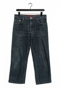 Jeans in denim blu scuro con taglio dritto, cinque tasche, rivetti in rame e un accento rosso sulla vita, appesi a un gancio nero.