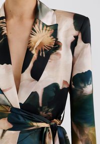 Σακάκι με λουλουδάτο μοτίβο από απαλό σατέν ύφασμα· διαθέτει βαθύ ντεκολτέ, μακριά μανίκια και ζώνη στη μέση που δένει. Χρώματα: μαύρο, πράσινο και μπεζ.