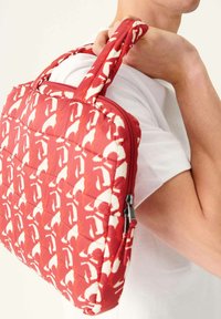 Rode gewatteerde tas met witte abstracte patronen, met dubbele handvatten en een rits sluiting, die door een persoon op de schouder wordt gedragen.