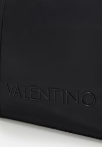 Svart nylonväska med en präglad "VALENTINO"-logotyp. Slät textur med en elegant design och en strukturerad form. Inga andra anmärkningsvärda detaljer.