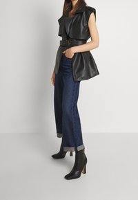 Svart väst i konstläder med bälte i midjan, tillsammans med blå vid jeans med uppvikta fållar och svarta klackiga ankelboots.