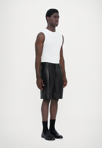 Top sans manches blanc à côtes, shorts en cuir noir avec des plis, et mocassins noirs avec des chaussettes. Design moderne et simple, ajustement sur mesure.