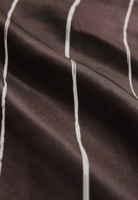 Brauner Stoff mit weißen vertikalen Streifen, glatter Textur und einem sanften Glanz, der sanfte Falten und Drapierungen zeigt.