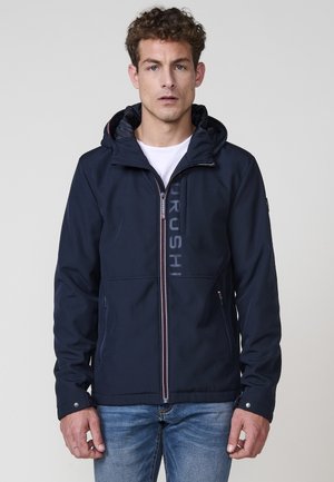 Chaqueta azul marino con cremallera frontal, capucha ajustable y detalle de logo, con una textura suave y dos bolsillos laterales.