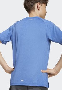 Modré sportovní tričko s krátkým rukávem vyrobené z texturované látky, s kulatým výstřihem a reflexním akcentem vzadu u límce.