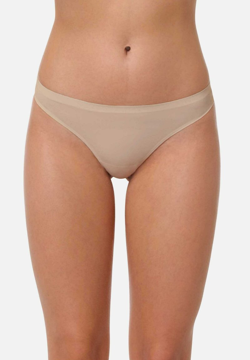 Culotte en tanga beige avec une texture lisse, offre une couverture minimale et une taille basse, conçue pour un ajustement sans couture.