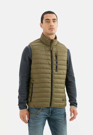 Gilet matelassé vert olive avec col montant, fermeture éclair et poches latérales, superposé sur une chemise à manches longues bleu foncé. Texture lisse, design matelassé.