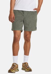 Olijfgroene shorts van zachte stof met een elastische tailleband, voorzien van zijzakken en een klein logo-embleem aan de zoom.