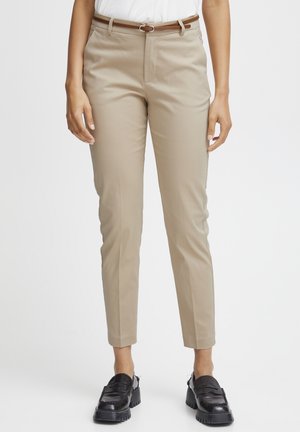 Pantaloni beige su misura con una cintura marrone, indossati con una camicia bianca. Il modello indossa scarpe con tacco nero su uno sfondo neutro.