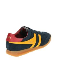 Marineblaues Wildleder-Sneaker mit rotem Absatz und gelben Streifen. Verfügt über eine Gummisohle und ein Logo auf der Ferse, was ein retro-athletisches Design bietet.