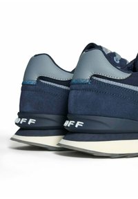 Ett par marinblå och grå sneakers visade från baksidan med vit text "OFF" på den svarta mellansulan och lager av krämfärgade och grå yttersulor.