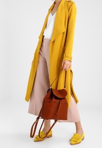 Lungo cappotto giallo con una texture a coste, abbinato a culotte rosa. Include una borsa a tracolla in pelle marrone e mocassini gialli.